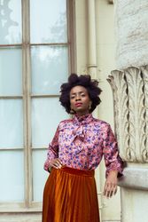 Woman in blue and pink floral top and brown skirt standing indoor