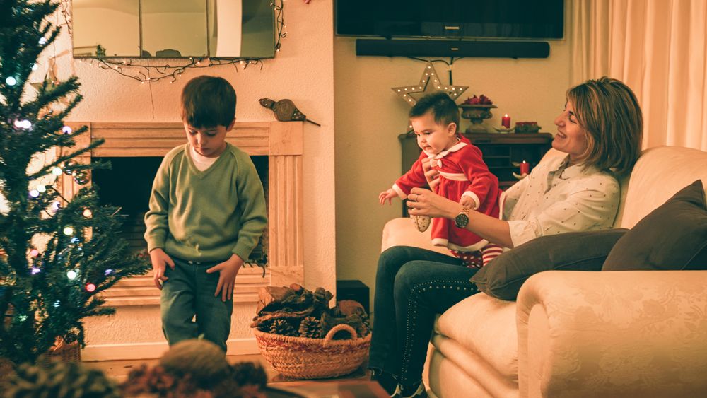Mother playing with baby while son decorating Christmas tree