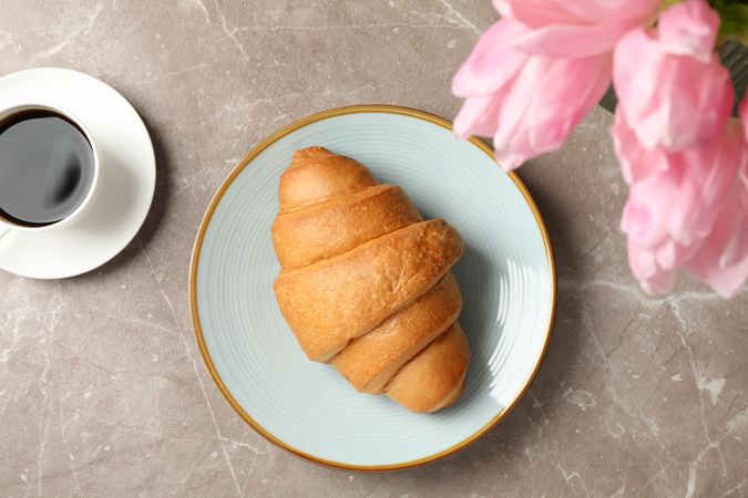Plate with croissant on grey background with tulips and cup of coffee, with space for text