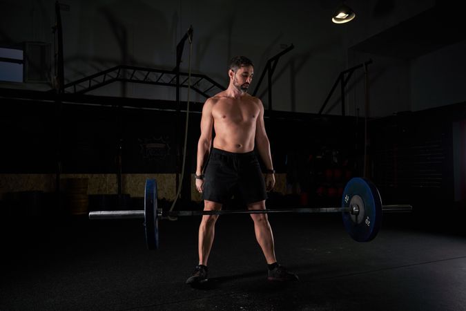 Muscular strong man preparing for lifting barbell with weights