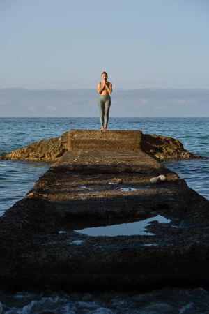 Slim woman standing on stone pier in sea