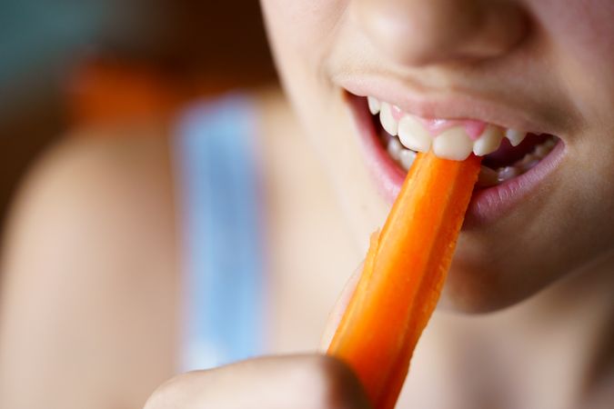 Anonymous teenage girl taking a bite of carrot stick
