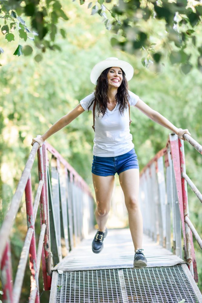 Carefree brunette female swinging herself on wooden bridge in forest