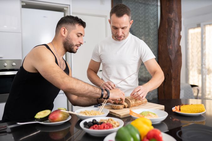 Male couple preparing vegetables and cutting bread for sandwich