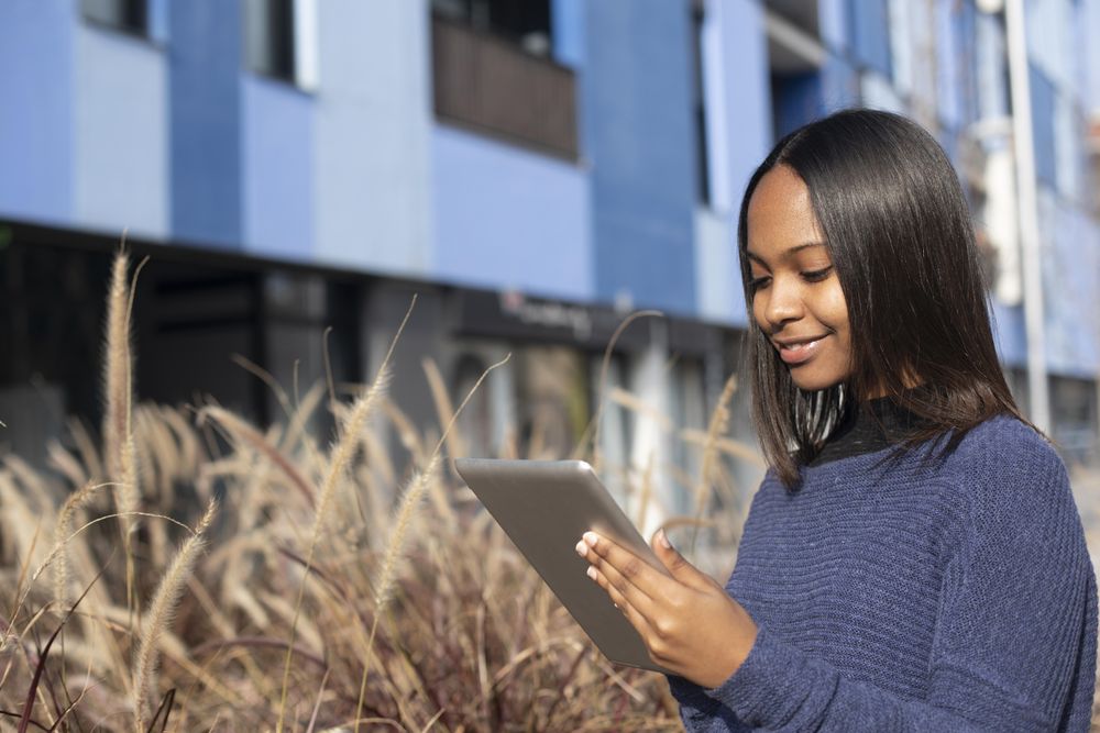Female in sweater standing outside blue building with tablet