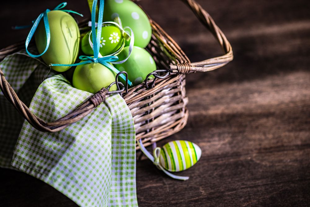 Colorful eggs in basket and pussy willow branches on wooden table