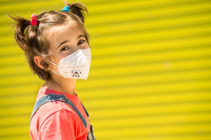 Cute girl in protective mask against a yellow wall