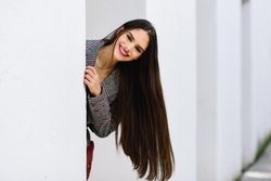Smiling female peaking out from behind light wall outdoors