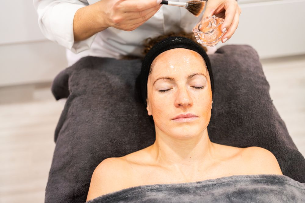 Cosmetologist brushing product on female client's forehead
