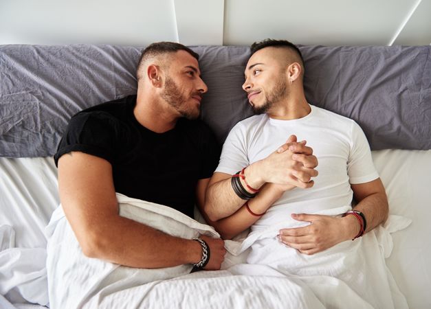 Smiling gay couple hugging on bed