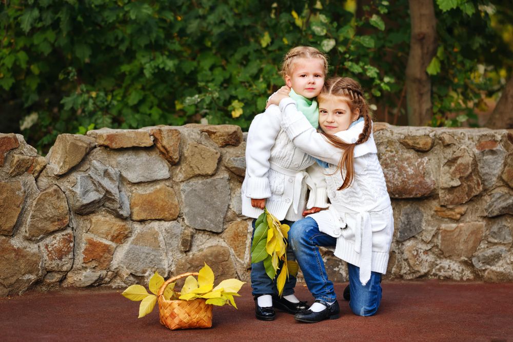 Big sister hugging her little sister in front of stone wall in park