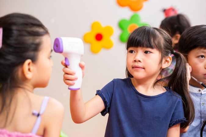 Asian girl playing as doctor using infrared thermometer