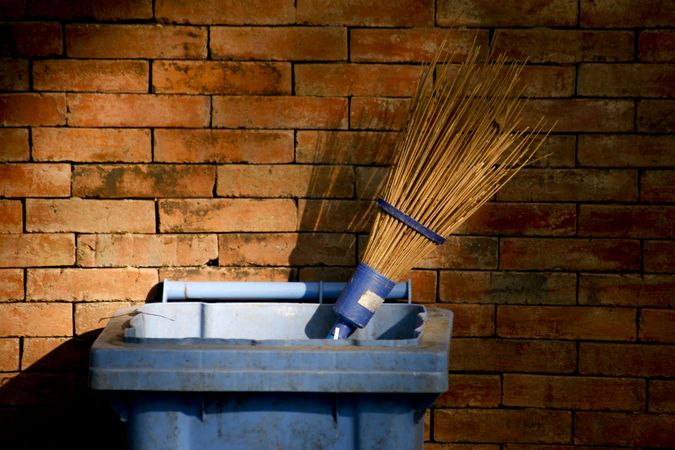 Garbage bin with broom against brick wall