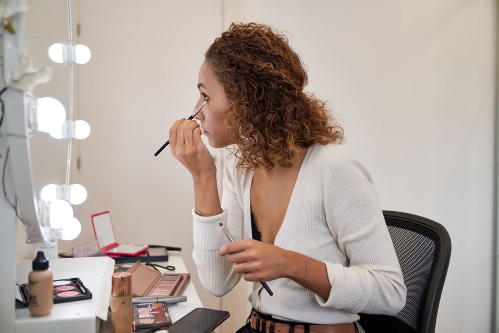 Young woman doing makeup near mirror