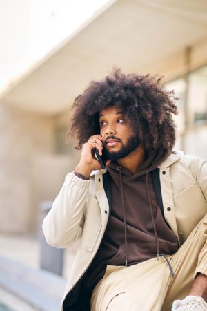 Young man with curly afro hair on the street talking on the cell phone
