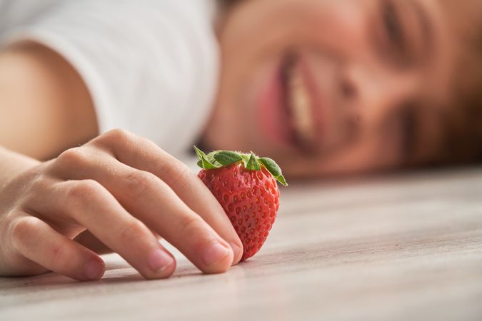 Crop kid lying on floor with strawberry