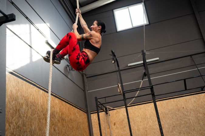 Fit woman climbing a rope in a gym