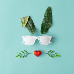 Bunny rabbit face made of green leaves with sunglasses and red heart on pastel blue background