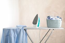 Iron and basket with clear laundry against light background, space for text