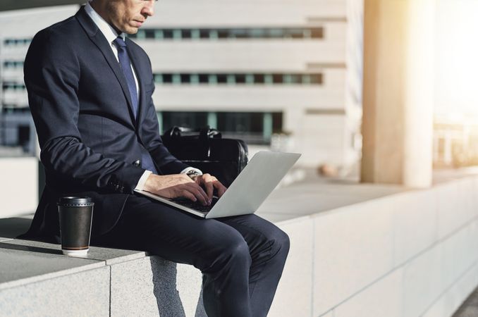 Man in smart business attire working on his laptop outside