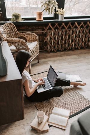 Side view of woman working on her laptop sitting on floor at home
