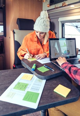 Male and female friends working remotely in back of van while camping, vertical