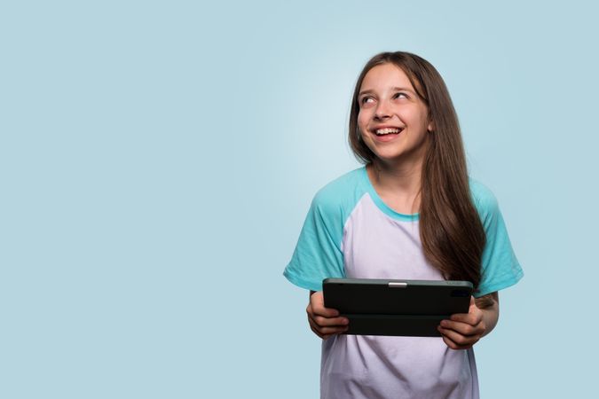 Smiling girl gazing upwards while holding tablet