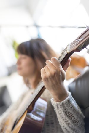 Female hand strumming acoustic guitar in bright loft, vertical