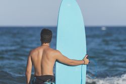 Male surfer with blue board standing in front of the ocean