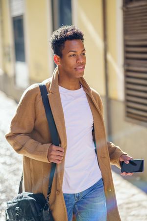 Cuban male strolling down street holding leather bag and phone, with rainbow lens flare
