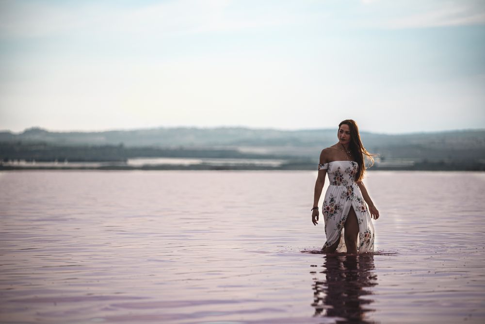 Peaceful woman in white dress walking ankle deep in pink lake