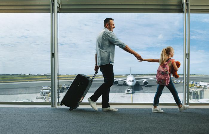 Girl holding hand of her father and walking to board their flight at airport