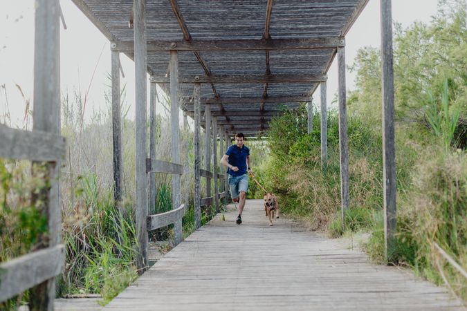 Happy adult man running with dog along countryside