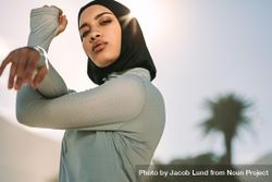 Young sportswoman in hijab stretching her arms and looking at camera 4BvV34