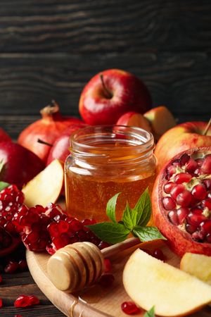 Apples on board with honey and pomegranate on dark wooden background, vertical