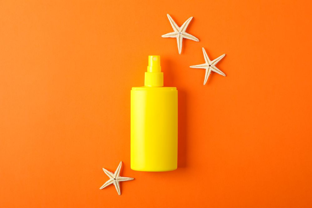 Composition with sunscreen spray and starfishes on color background, space for text. Summer vacation backdrop