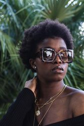 Confident Black woman in sunglasses against greenery