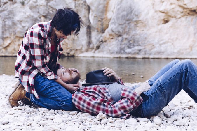 Positive woman and man resting on stone shore near river