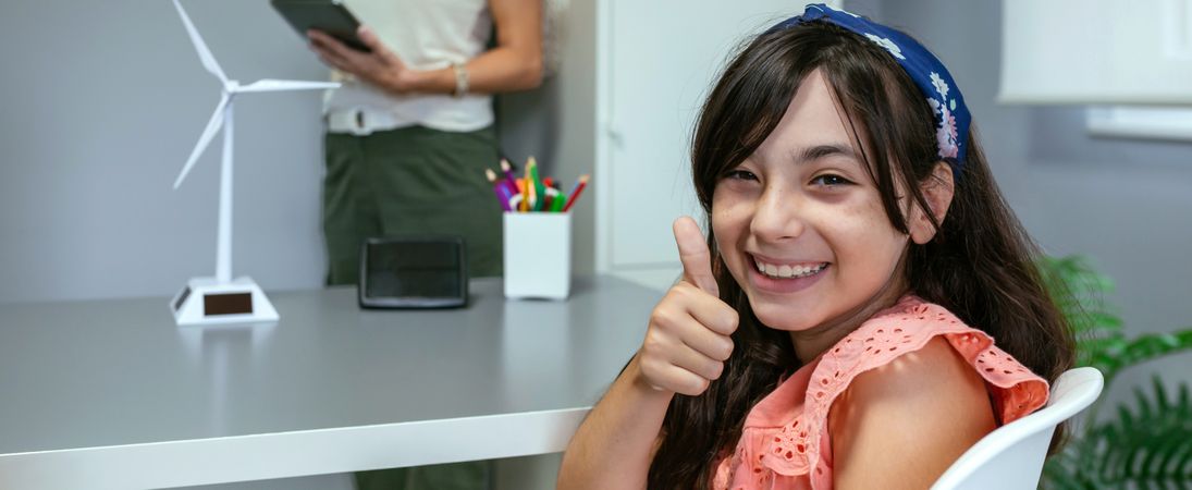 Portrait of schoolgirl in ecology classroom and teacher explaining lesson on background