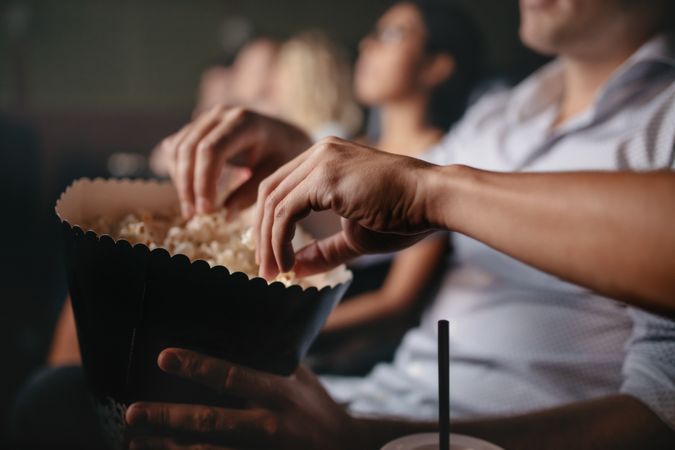 Close up shot of young people eating popcorn in movie theater, focus on hands