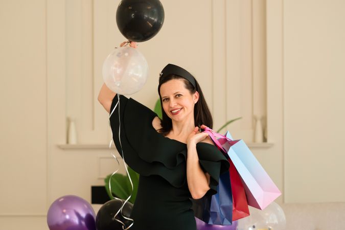 Woman with balloons and gift bags, celebrating indoors.