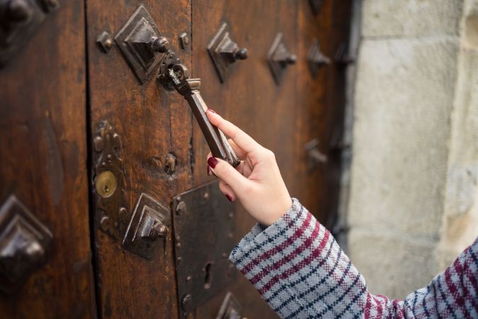 Curious female traveler in casual wear clattering in ancient door at city street
