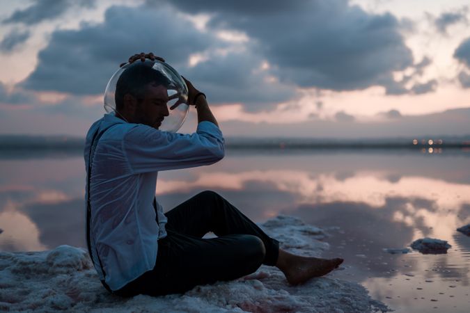 Man with fish tank on head sitting at seashore