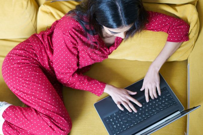 Woman relaxing at home using computer on yellow sofa