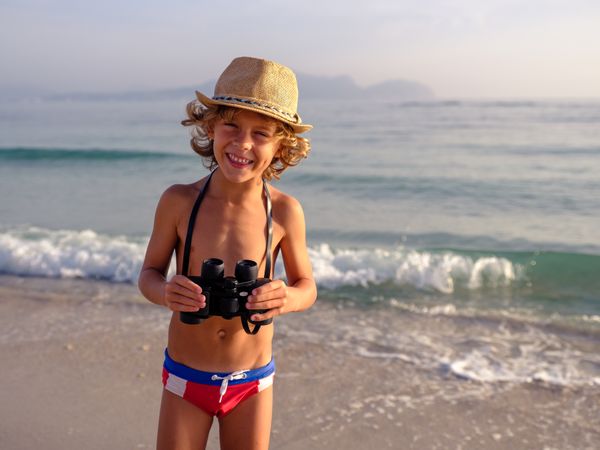 Smiling boy with binoculars standing on sandy beach