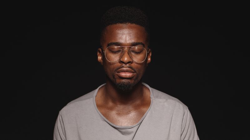 African male in eyeglasses and tshirt isolated on dark background with closed eyes