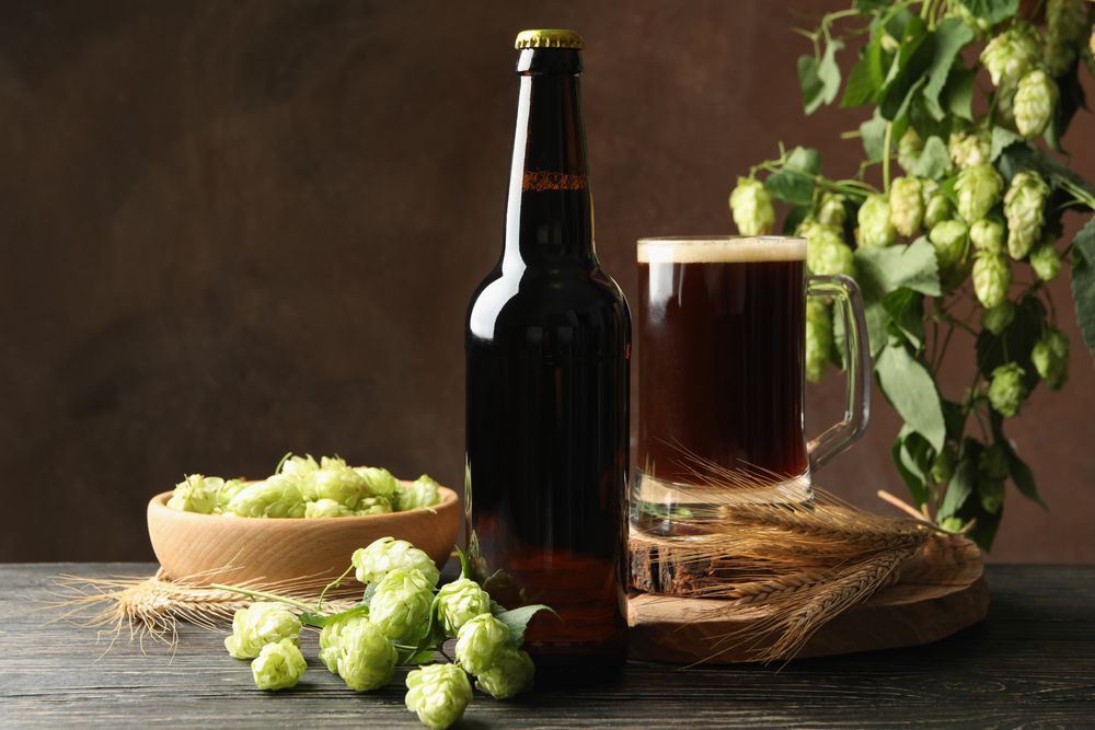 Beer, hop and wheat on wooden table against brown background