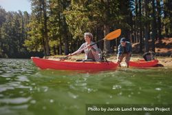 Portrait of mature woman canoeing in the lake with man about to catch the kayak from behind 0JNWn0