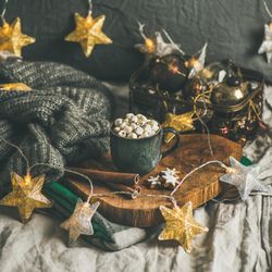 Hot drink with marshmallows in mug, in cozy warm setting with festive decorations, square crop