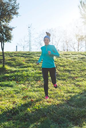 Woman in blue jogging on grass hill on sunny fall day